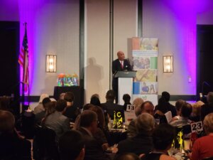 Dominic Carter delivering a keynote on child advocacy and resilience, sharing his journey from foster care and adversity to becoming a WABC Radio host and motivational speaker.